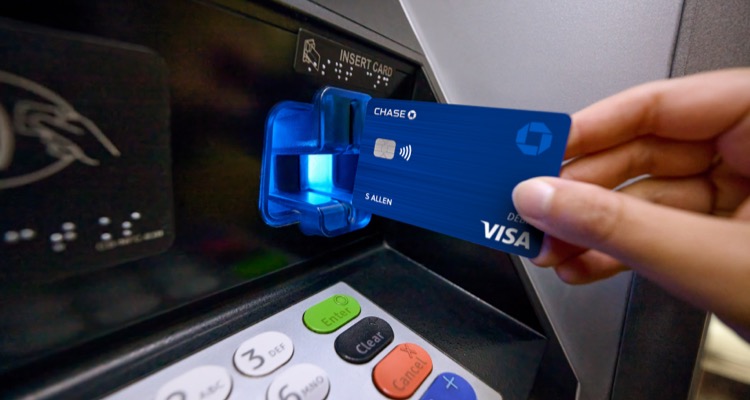 A hand inserts debit card into a Chase ATM machine to withdraw money