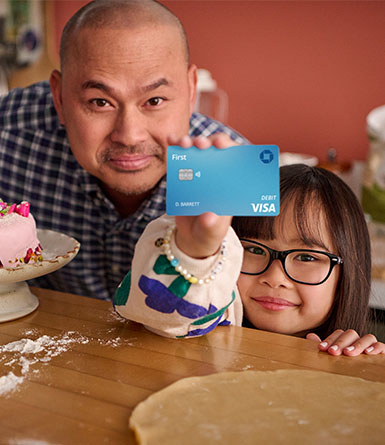 Una hija de pie junto a su padre mostrándole su tarjeta de débito de Chase First Banking